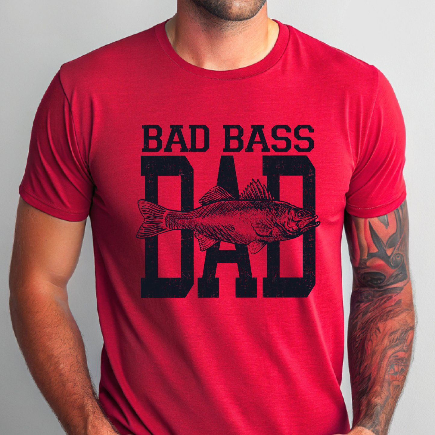 Bad Bass Dad fishing shirt featuring a vintage distressed text design with a detailed bass fish graphic on red T-shirt.