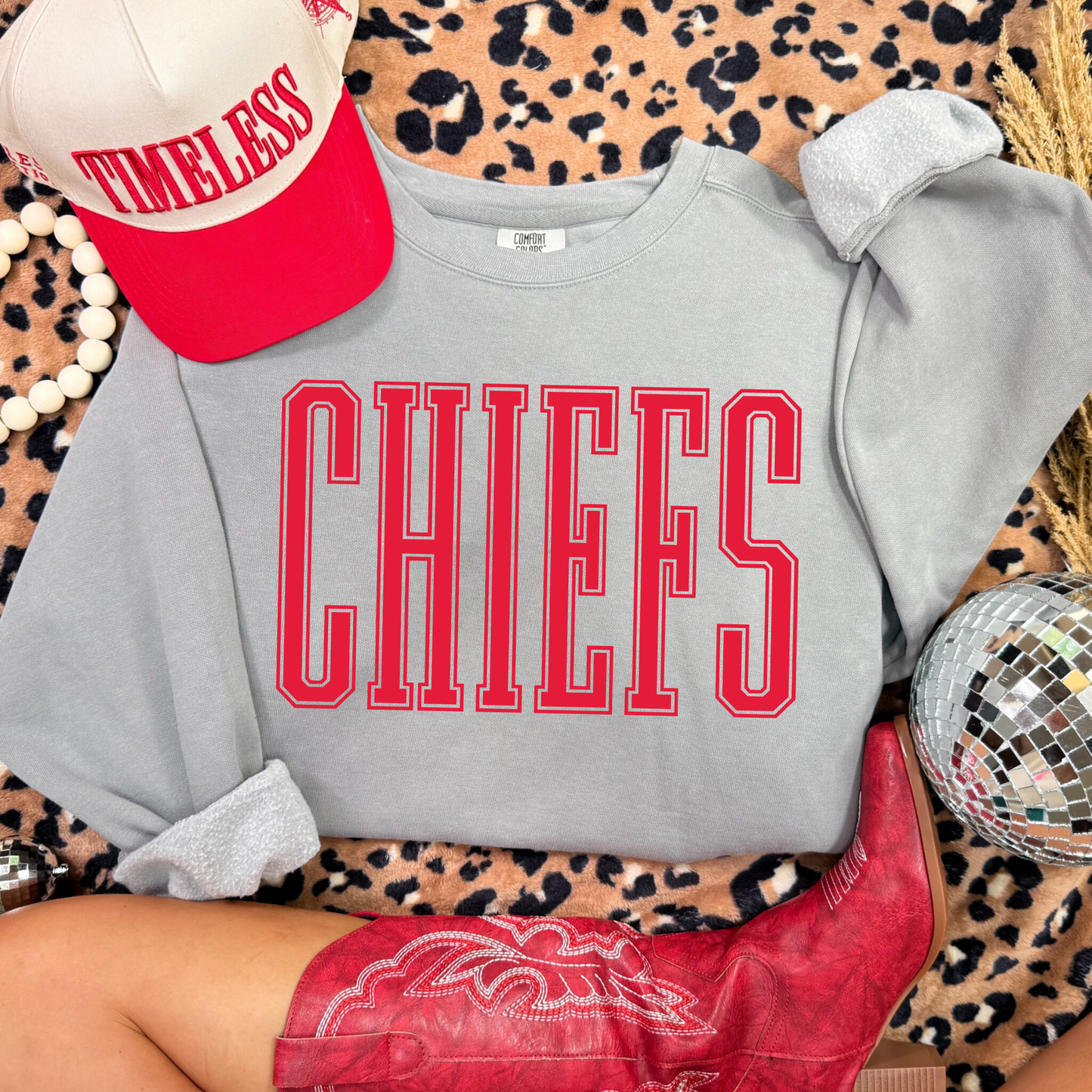 Gray Comfort Colors sweatshirt with 'CHIEFS' in red text, red cap, and red boots on a leopard print background.