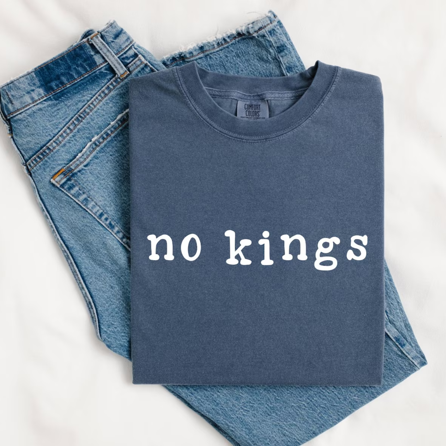 Folded navy Comfort Colors T-shirt with white typewriter text reading ‘no kings,’ styled next to denim jeans.