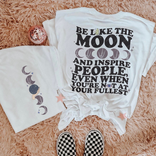 White graphic t-shirt featuring celestial moon phase artwork and inspirational quote that reads “Be Like the Moon and Inspire People, Even When You’re Not at Your Fullest” with trendy boho aesthetic styling.