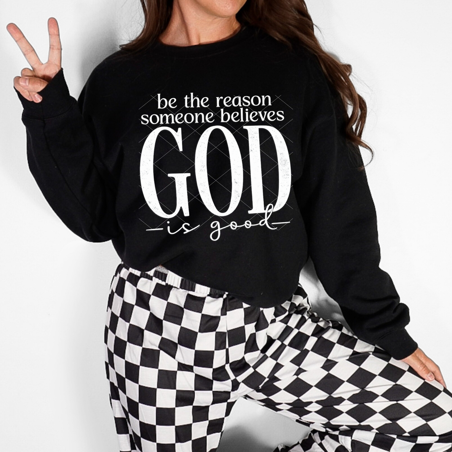 Woman wearing a black Christian sweatshirt with the quote ‘Be the reason someone believes God is good’ in white lettering.”