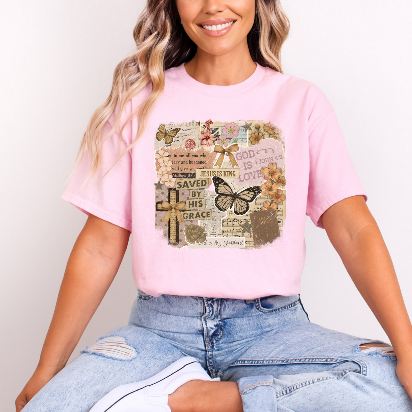Christian scrapbook graphic tee on light pink shirt with butterflies, florals, Bible verses, and vintage collage elements modeled seated casually.