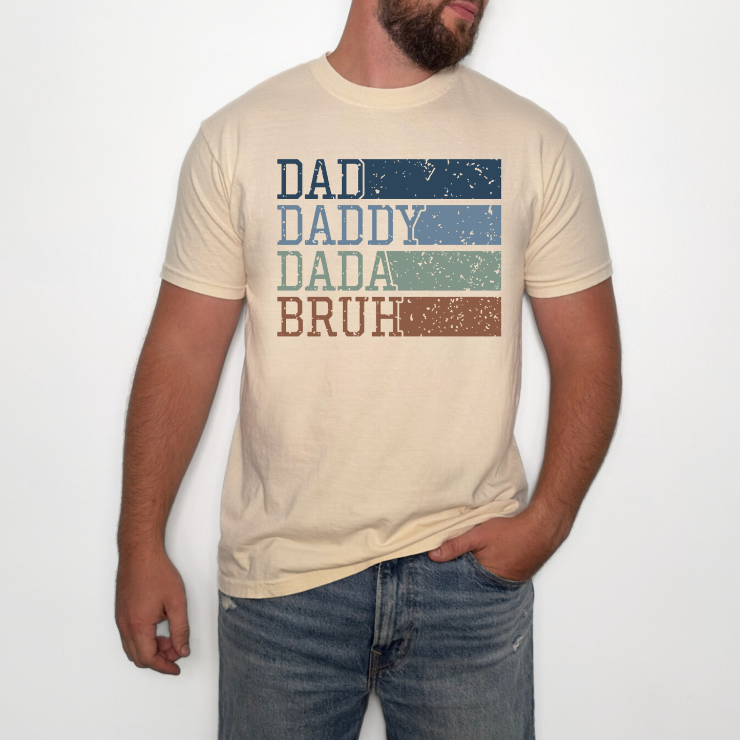 Person wearing a beige t-shirt with 'DAD DADDY DADA BRUH' text design on a plain background