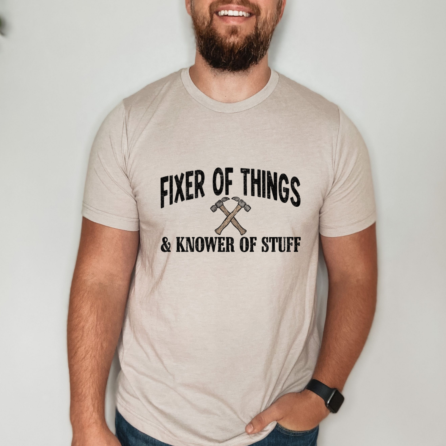 Vintage-inspired Fixer of Things and Knower of Stuff shirt featuring crossed hammers and distressed typography on a soft gray tee.