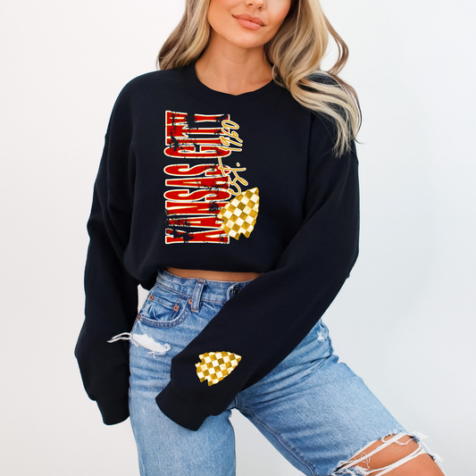 Model wearing Kansas City Est. 1960 vertical crewneck sweatshirt in black with red lettering and gold checker arrowhead graphics.