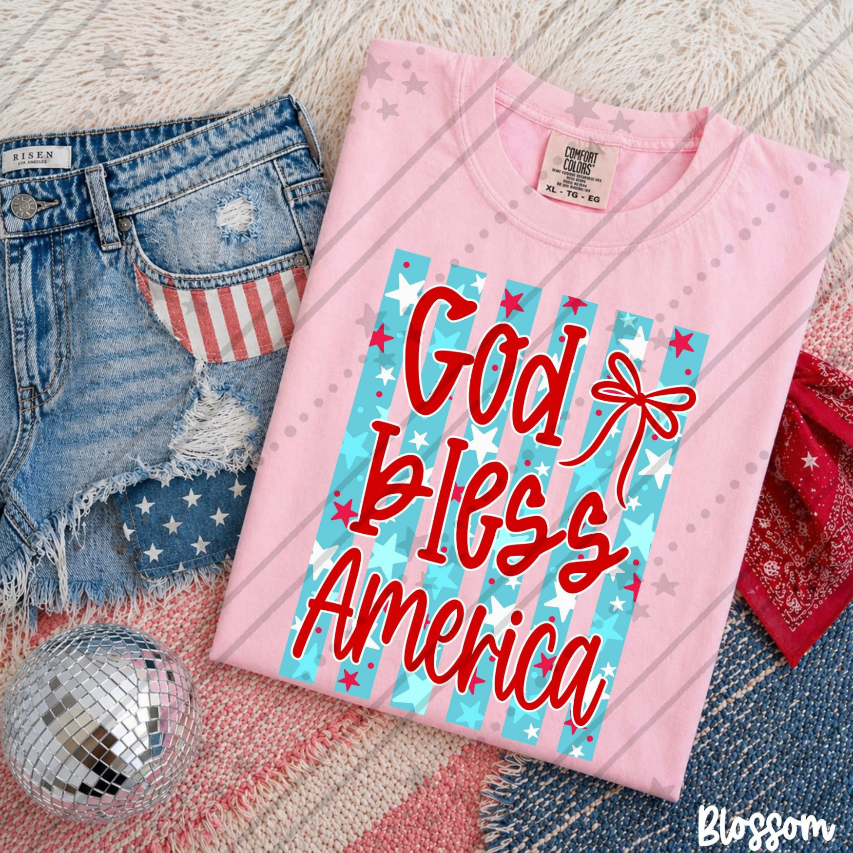 God Bless America Stars & Stripes patriotic Comfort Colors graphic tee in pink and blue with red lettering and Americana design.
