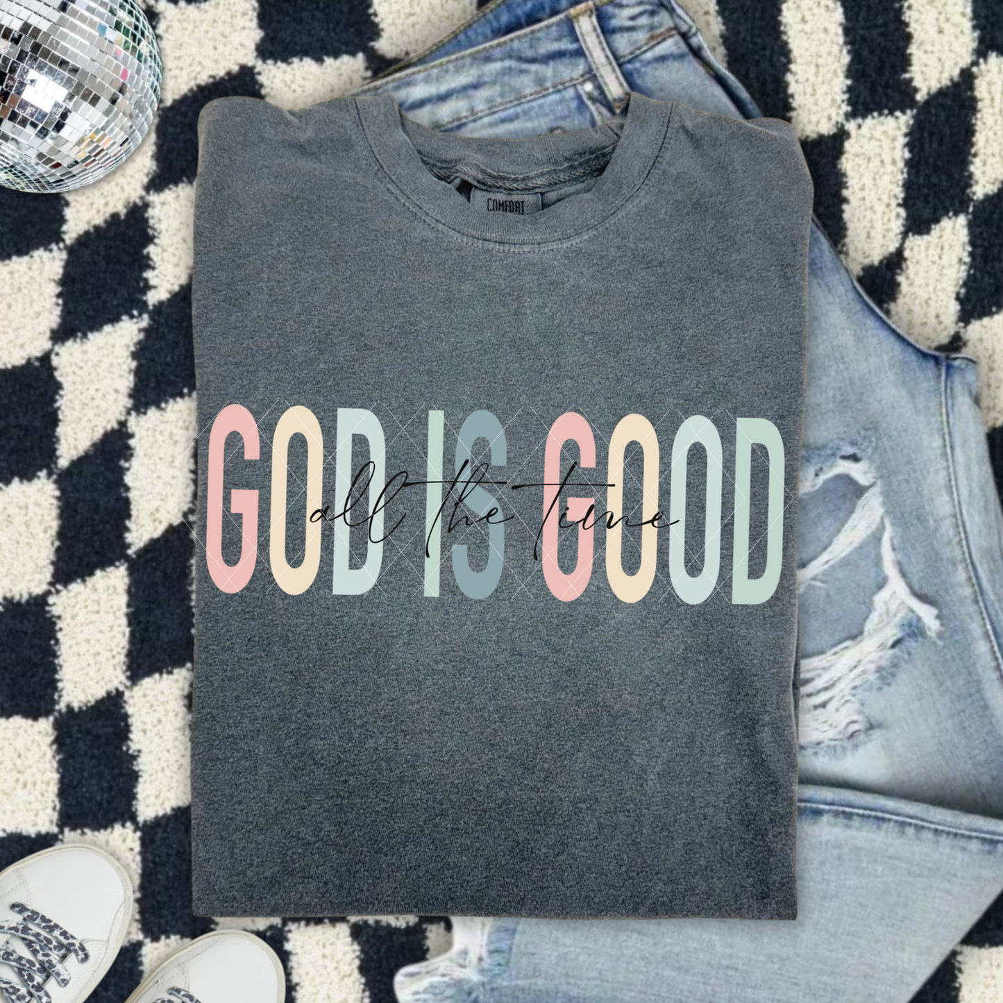 God Is Good All The Time sweatshirt in Comfort Colors Pepper with pastel lettering, displayed with jeans on a patterned rug