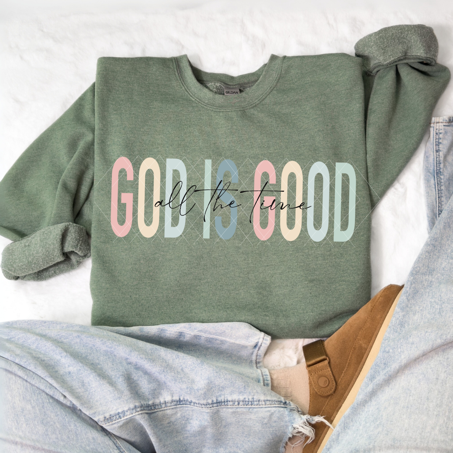 God Is Good All The Time sweatshirt in Gildan Heather Dark Green featuring pastel lettering, flat-lay with denim and slippers.