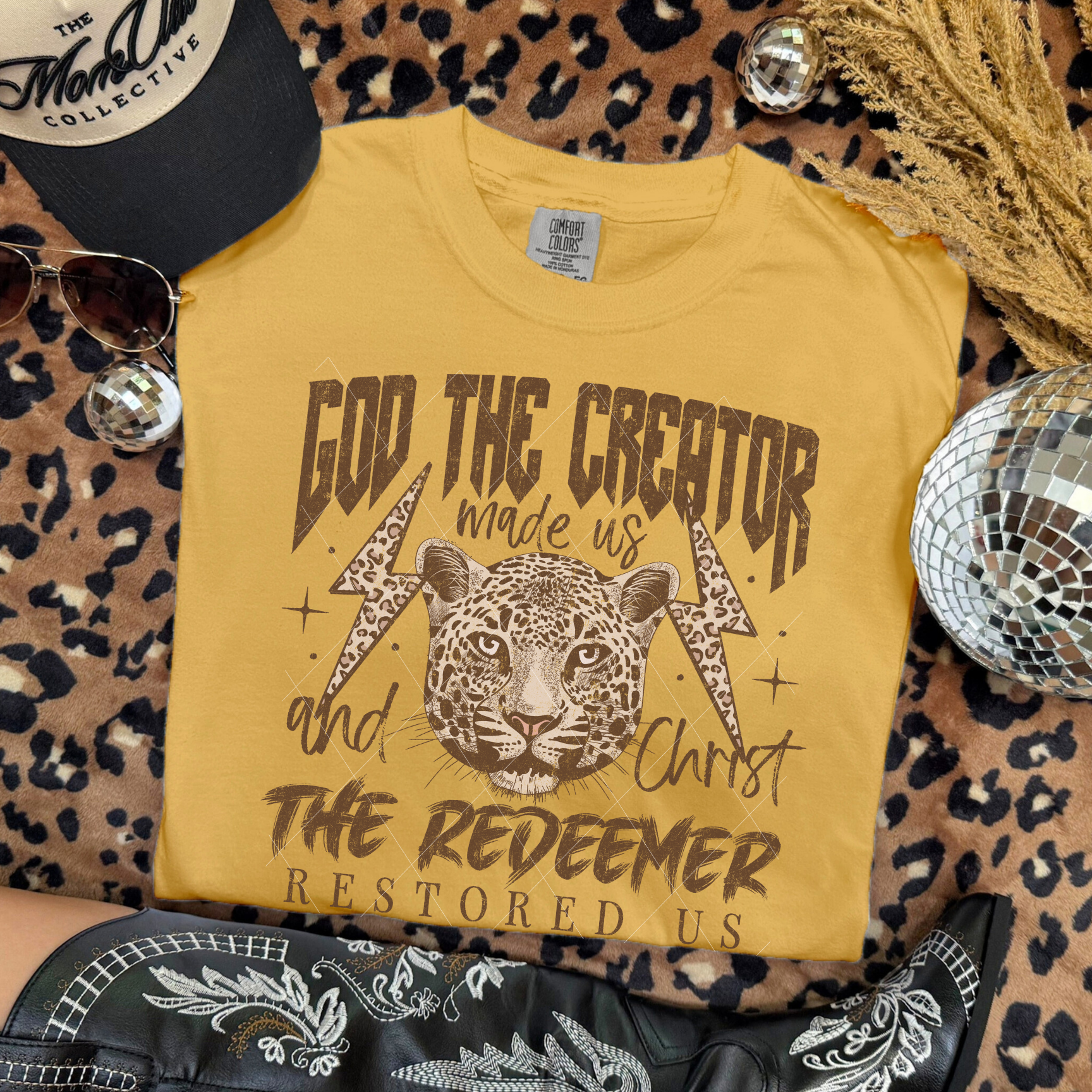 God the Creator Christ the Redeemer tee in Mustard with bold leopard illustration and faith message, styled with Western boots and accessories.