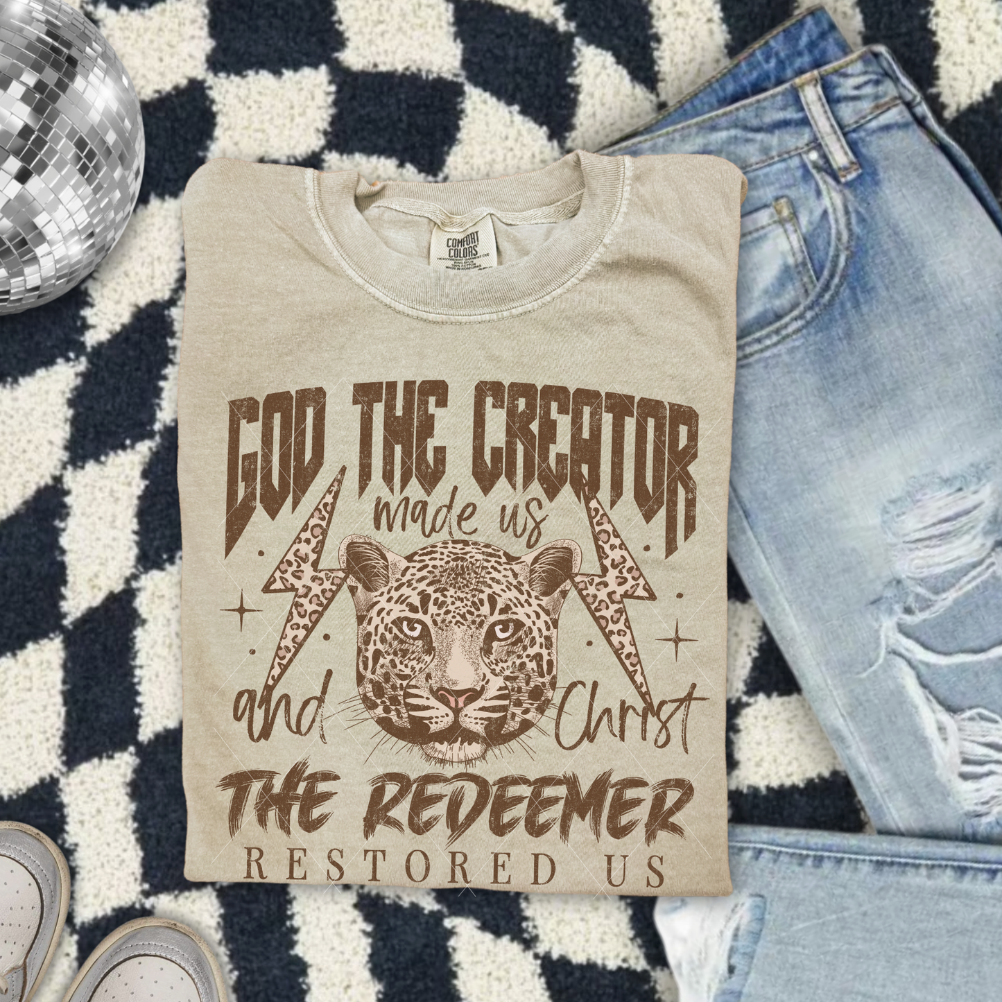 God the Creator Christ the Redeemer tee in Khaki, vintage-style Christian design with leopard graphic displayed with denim jeans.