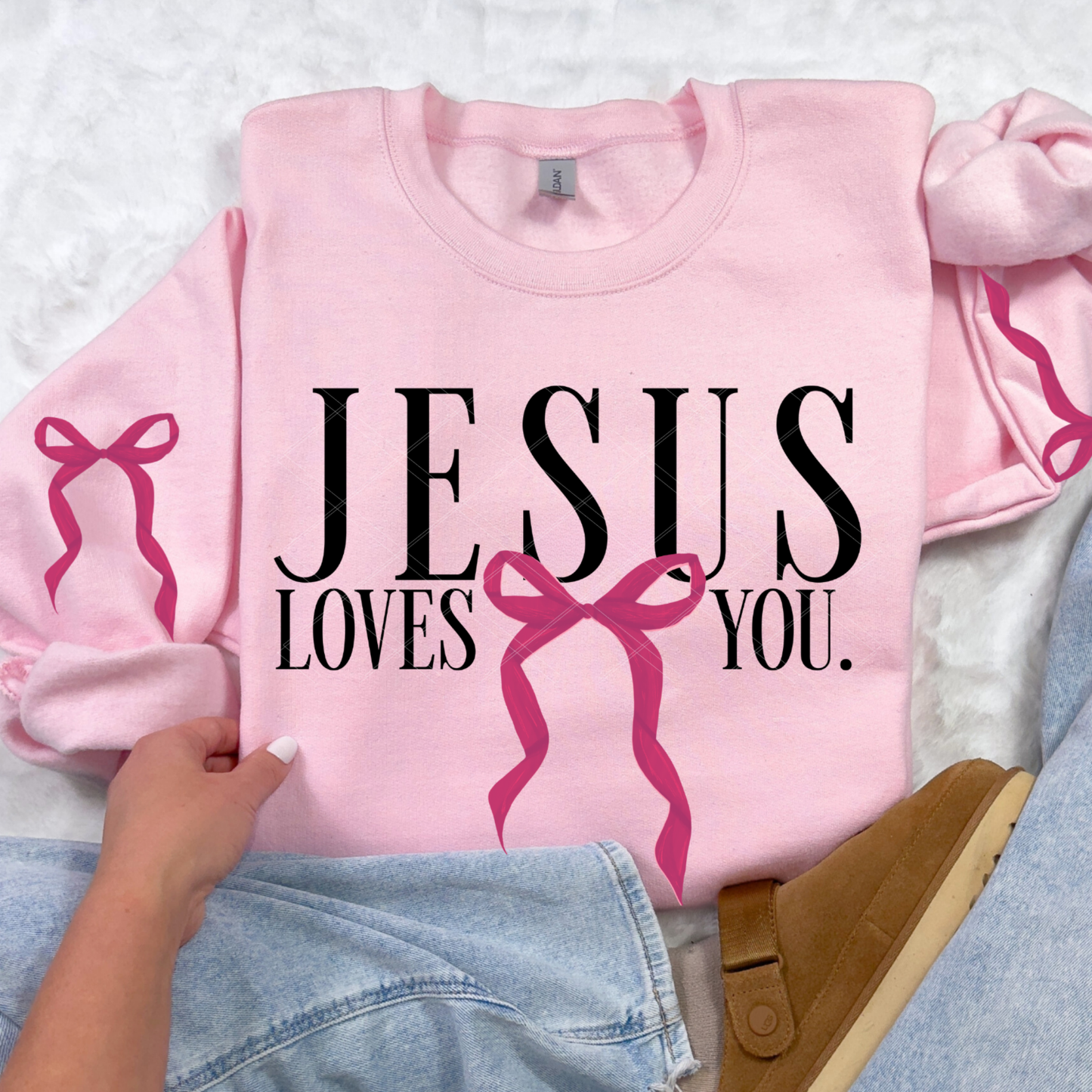 Light pink Jesus Loves You sweatshirt with painted bow design on front, styled with jeans and slippers.