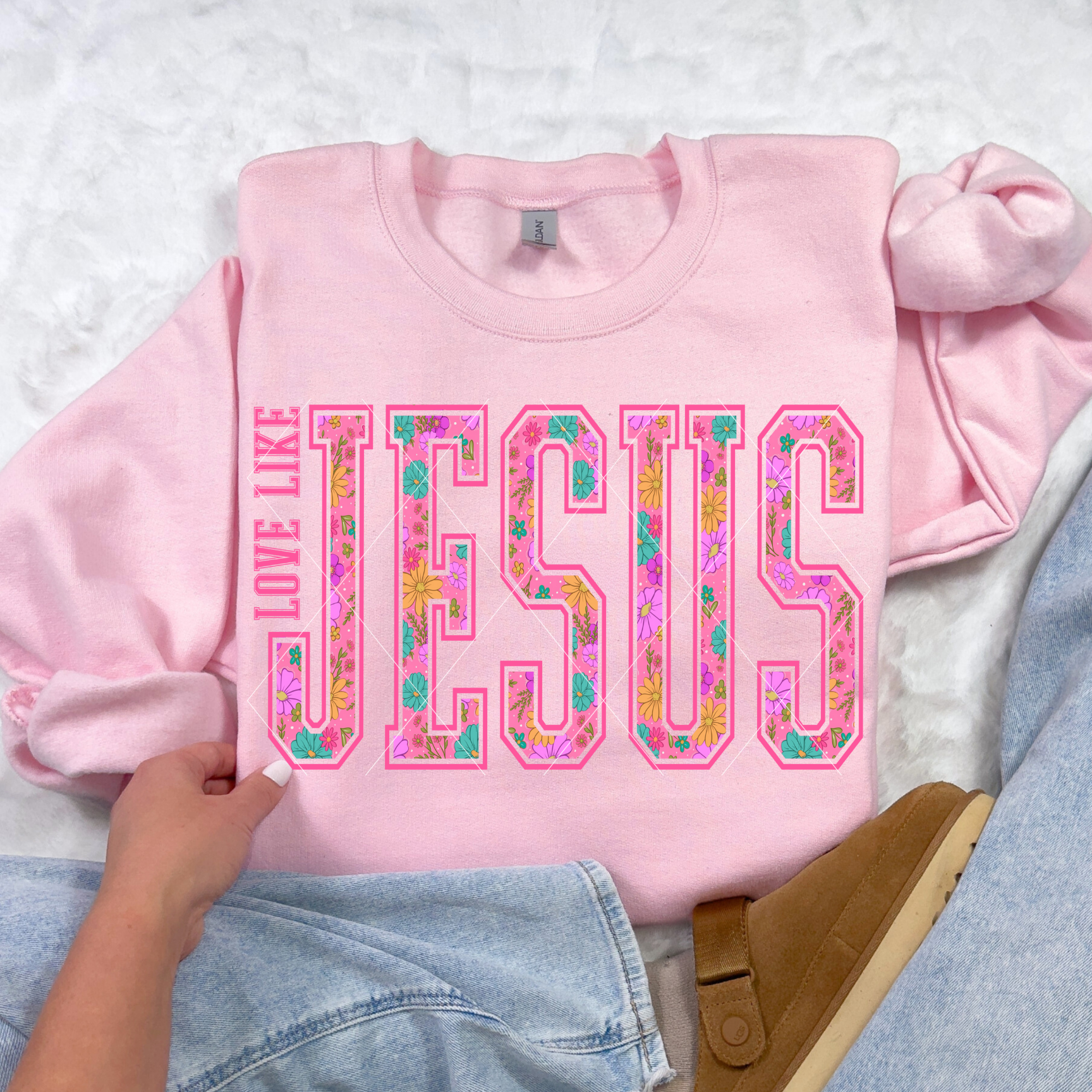 Light pink Love Like Jesus sweatshirt featuring bright floral varsity lettering in flat-lay with denim