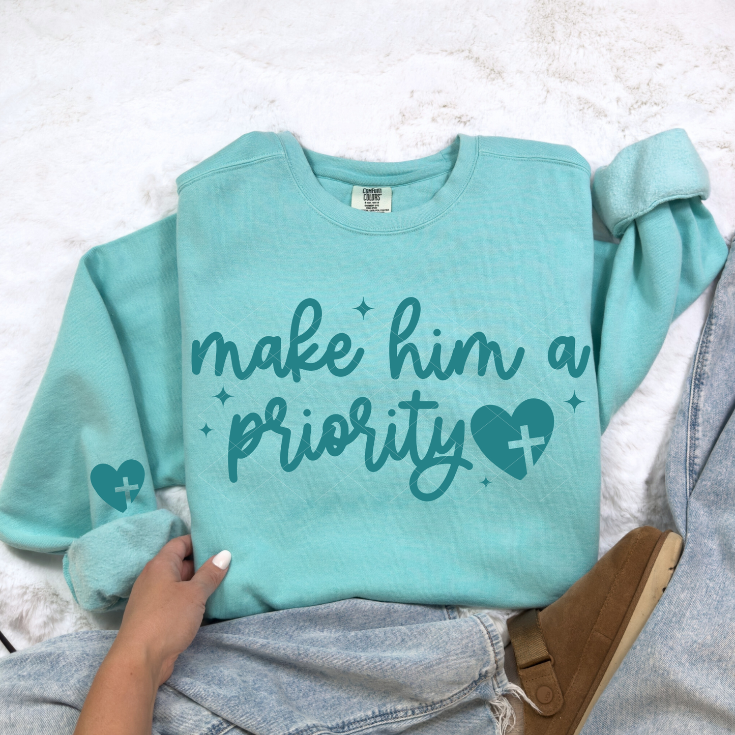 Chalky mint Make Him a Priority Christian sweatshirt with teal script lettering and heart-cross design, styled with denim.