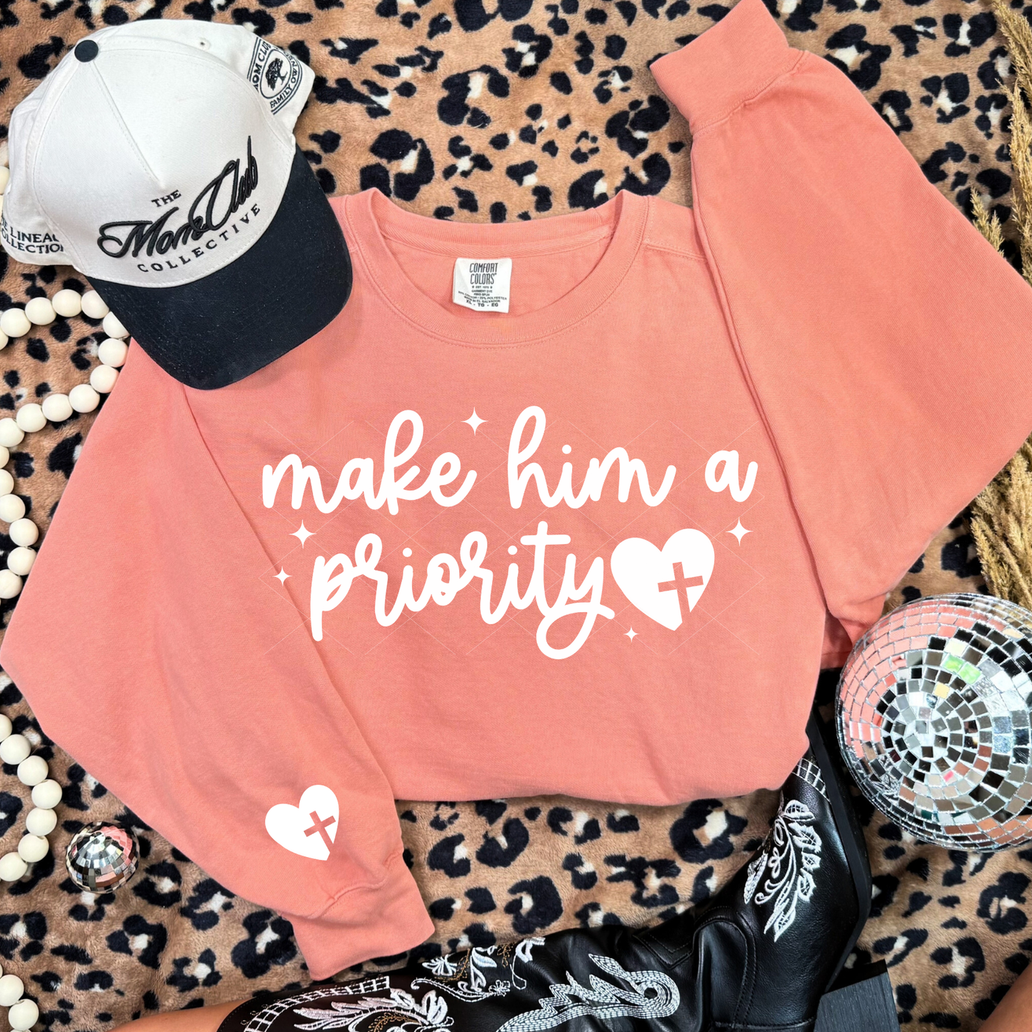 Terracotta Make Him a Priority sweatshirt with white script and heart-cross graphic on leopard backdrop.