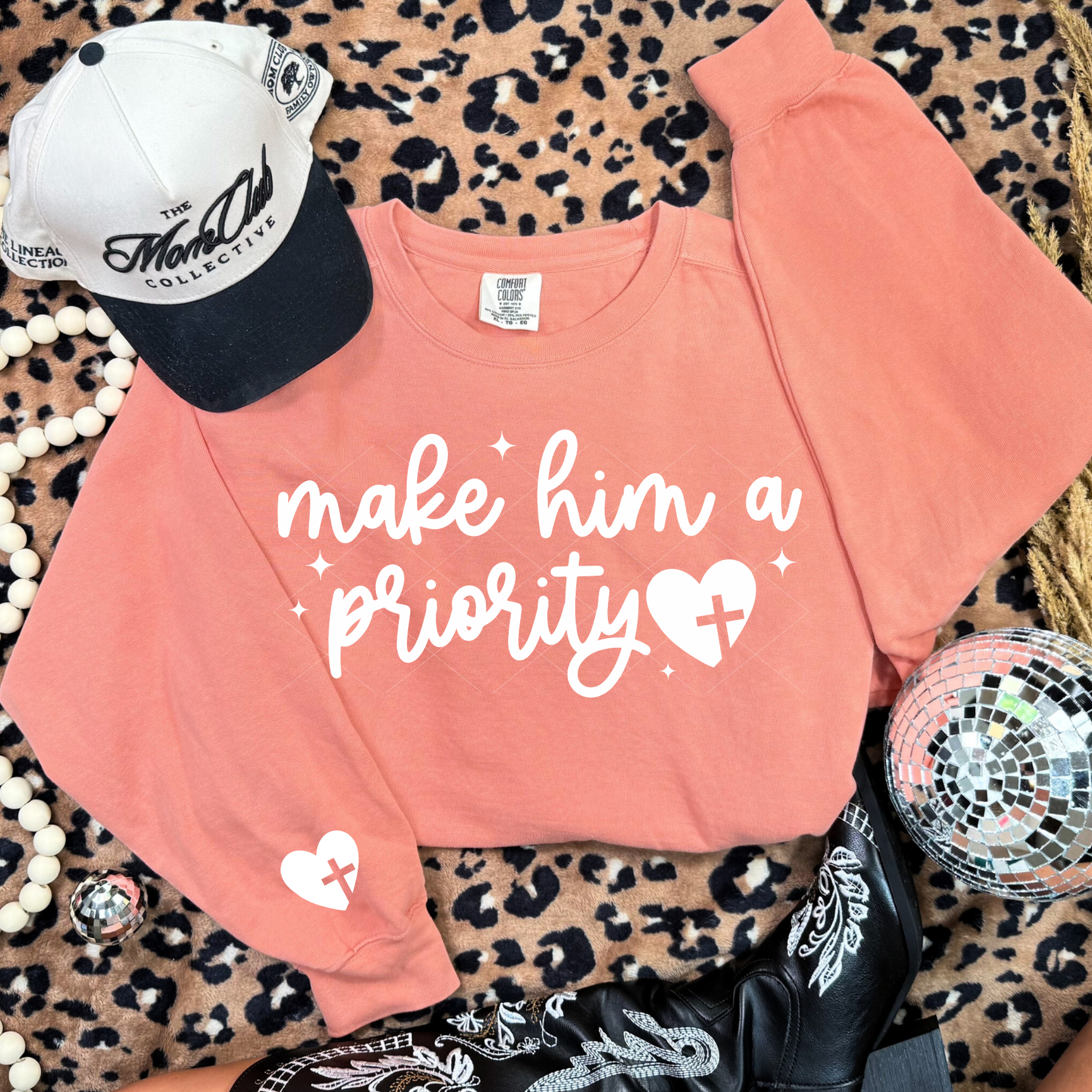 Terracotta Make Him a Priority sweatshirt with white script and heart-cross graphic on leopard backdrop.