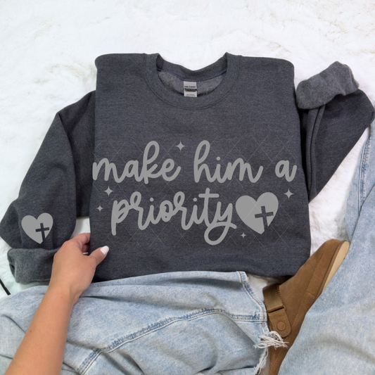 Dark heather gray Make Him a Priority sweatshirt with gray script and heart-cross detail, styled in flat-lay with denim.