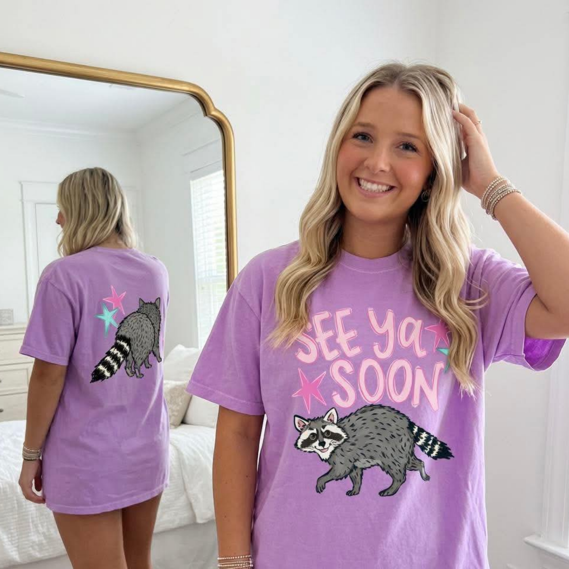See Ya Soon Raccoon lavender graphic tee featuring cute raccoon artwork on the front and back with pastel star accents.