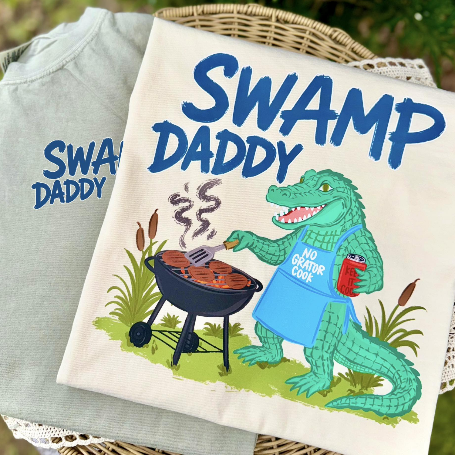Funny Swamp Daddy shirt featuring a grilling alligator wearing a barbecue apron and cooking burgers on a charcoal grill.