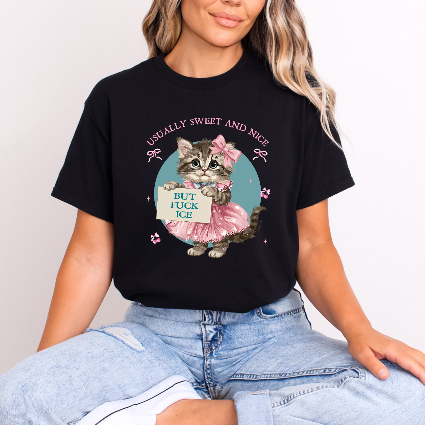 Woman wearing black T-shirt with vintage kitten graphic and text ‘Usually Sweet and Nice, But F*ck ICE,’ sitting casually in jeans.